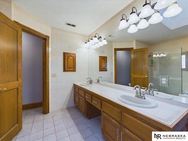 bathroom with a sink, visible vents, tile walls, and a textured ceiling