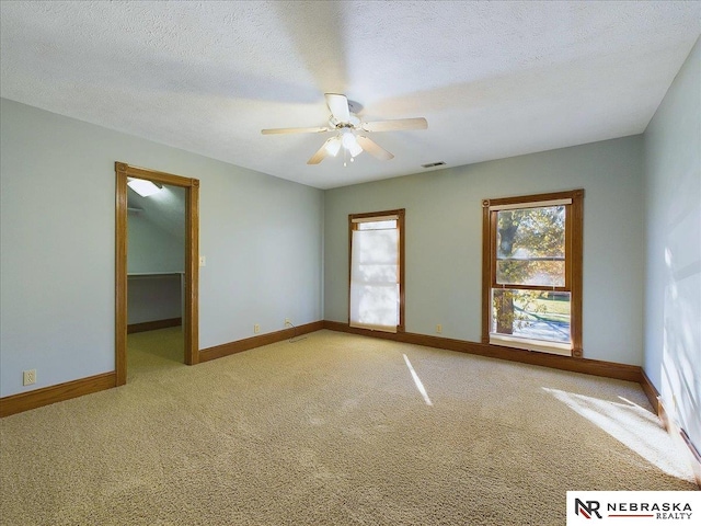 empty room with light colored carpet, baseboards, a textured ceiling, visible vents, and a ceiling fan