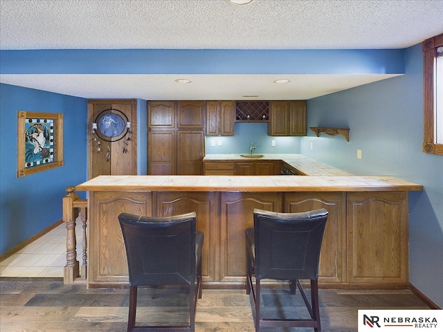 kitchen featuring a breakfast bar, a textured ceiling, a sink, tile countertops, and a peninsula