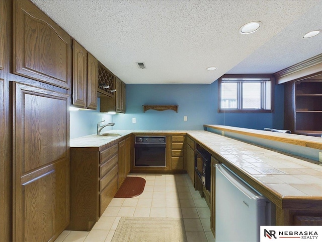 kitchen with a sink, tile counters, a textured ceiling, visible vents, and black appliances