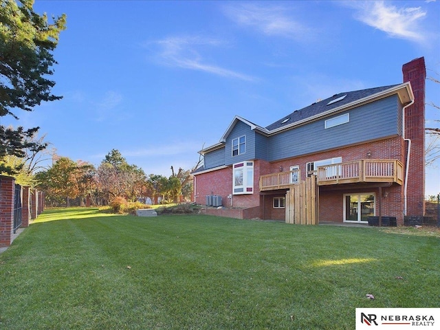back of house featuring central AC unit, a wooden deck, a chimney, brick siding, and a yard