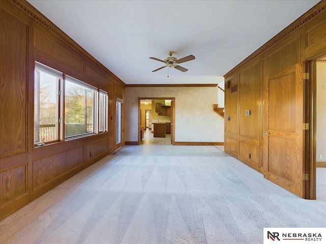 unfurnished living room with baseboards, ceiling fan, crown molding, and light carpet
