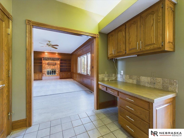 kitchen featuring built in study area, light countertops, a ceiling fan, brown cabinetry, and a fireplace