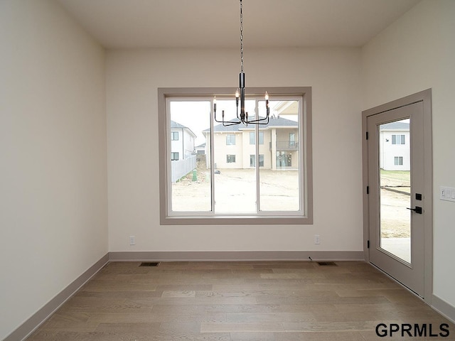 unfurnished dining area with a wealth of natural light, visible vents, light wood-style floors, and an inviting chandelier