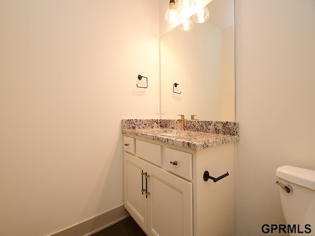 half bathroom with baseboards, toilet, and vanity
