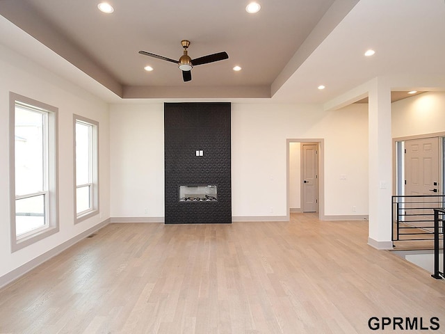 unfurnished living room with baseboards, a tray ceiling, a ceiling fan, and light wood finished floors