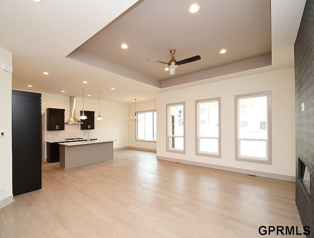 living room with a tray ceiling, light wood finished floors, and a ceiling fan