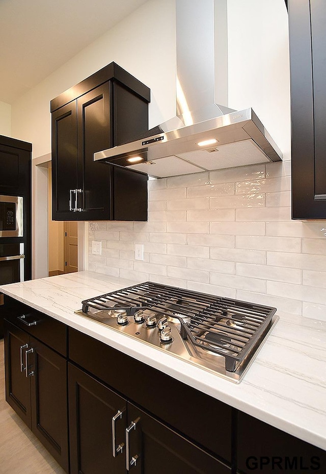 kitchen featuring decorative backsplash, wall chimney exhaust hood, light stone counters, and appliances with stainless steel finishes