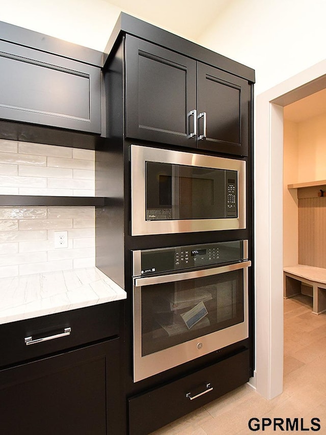 kitchen featuring backsplash, open shelves, light stone countertops, stainless steel appliances, and dark cabinets