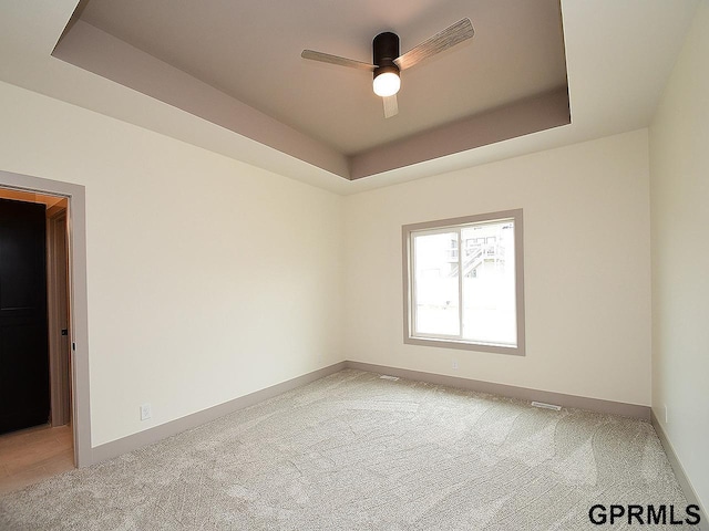 unfurnished room with light carpet, baseboards, a ceiling fan, and a raised ceiling