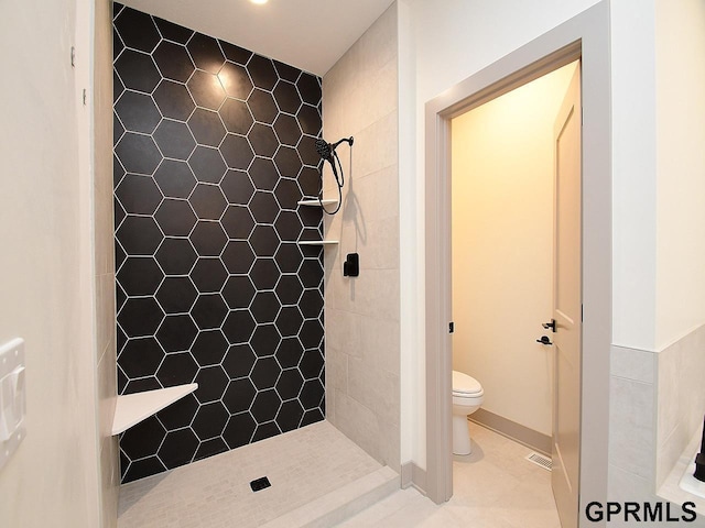 full bath featuring tile patterned floors, a tile shower, toilet, and baseboards