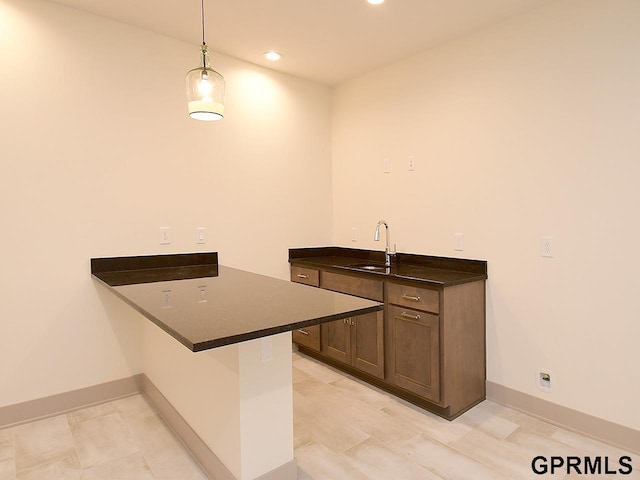 kitchen with a sink, a peninsula, hanging light fixtures, dark countertops, and recessed lighting