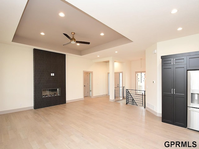 unfurnished living room featuring ceiling fan, recessed lighting, light wood finished floors, and a raised ceiling