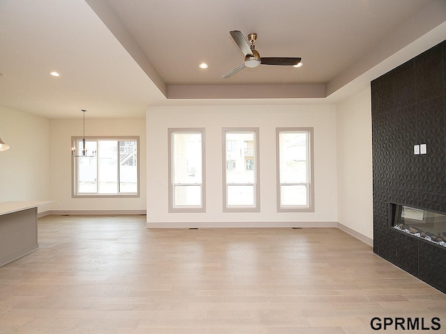 unfurnished living room with light wood finished floors, ceiling fan with notable chandelier, baseboards, and a large fireplace