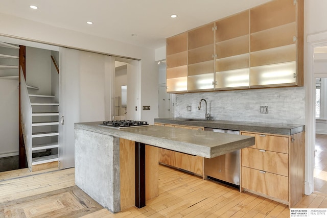 kitchen with a sink, light wood finished floors, tasteful backsplash, appliances with stainless steel finishes, and a center island