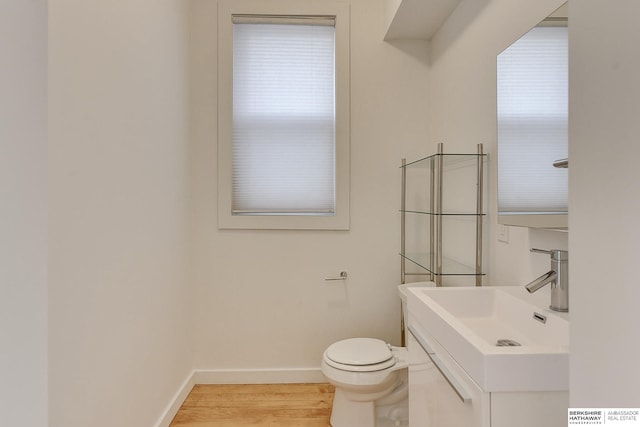 half bath featuring baseboards, toilet, wood finished floors, and vanity