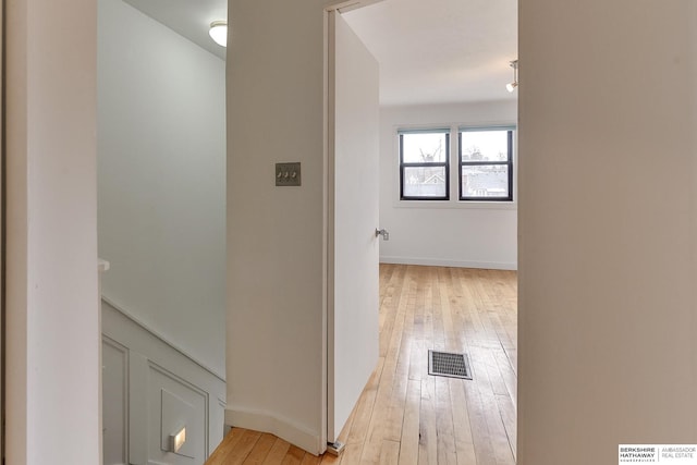 hallway featuring baseboards, light wood-style flooring, and visible vents