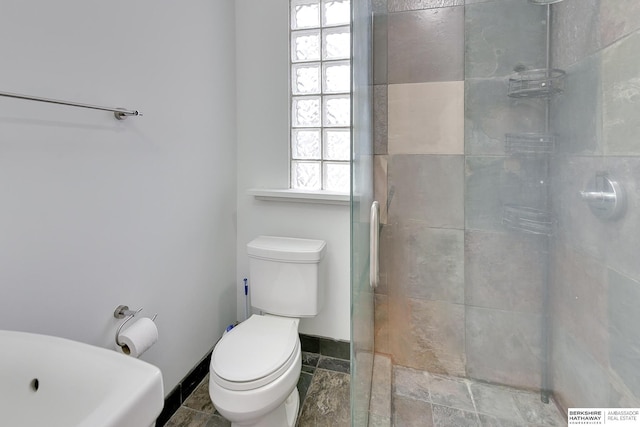 bathroom with toilet, baseboards, and tiled shower