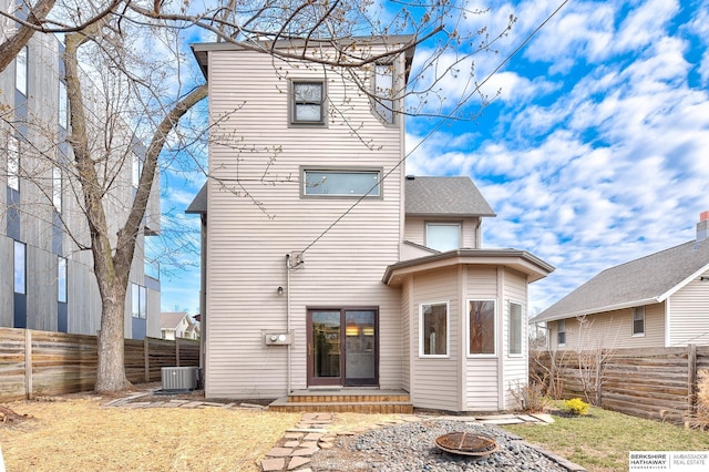 back of house with a lawn, central air condition unit, a fenced backyard, and a fire pit