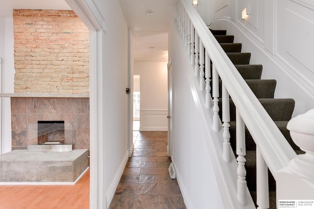 stairway with a tiled fireplace, a decorative wall, stone tile floors, and baseboards
