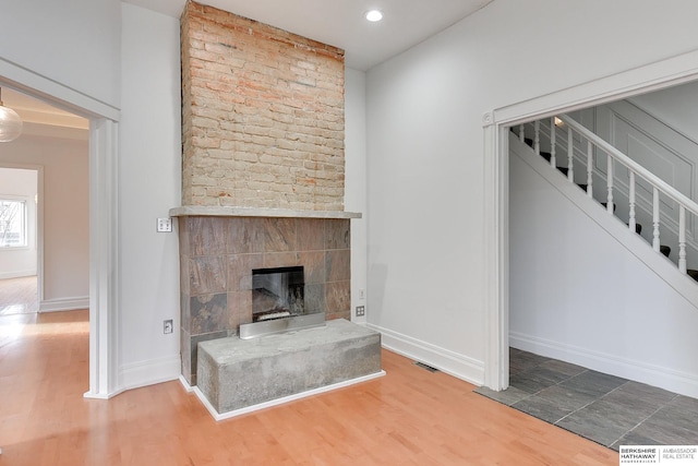 unfurnished living room featuring stairs, recessed lighting, baseboards, a fireplace, and wood finished floors