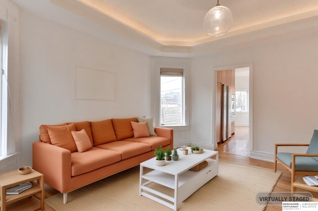 living room with baseboards, light wood-style floors, and a raised ceiling