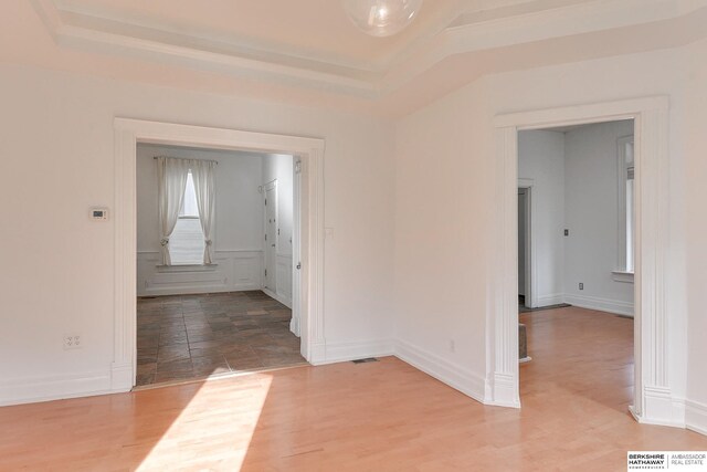 empty room with light wood finished floors, baseboards, visible vents, and a raised ceiling
