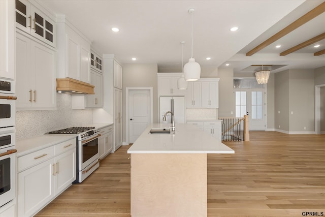 kitchen featuring light wood finished floors, a sink, a center island with sink, and white appliances