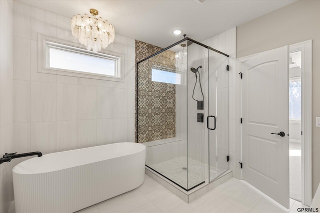 bathroom featuring a stall shower, tile patterned floors, a notable chandelier, a soaking tub, and tile walls