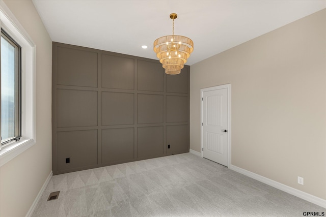 unfurnished room with plenty of natural light, light carpet, a decorative wall, visible vents, and a notable chandelier