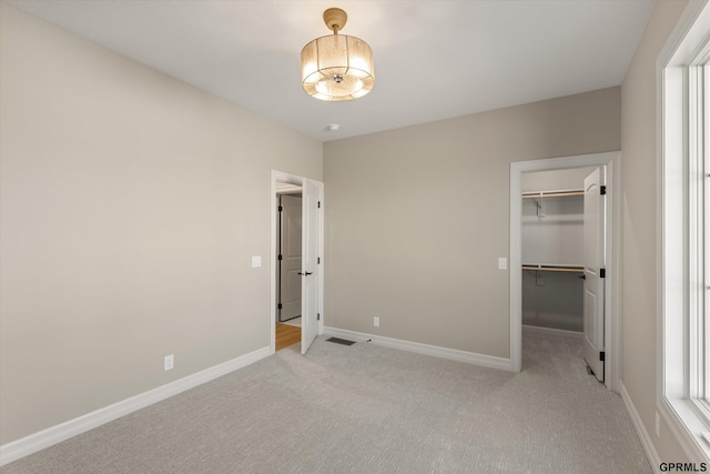 unfurnished bedroom with light colored carpet, a spacious closet, baseboards, visible vents, and a closet