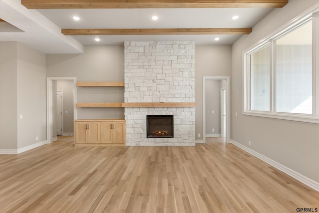 unfurnished living room featuring light wood finished floors, baseboards, a fireplace, and beam ceiling
