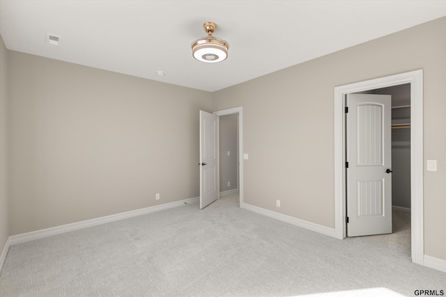 unfurnished bedroom with a spacious closet, light carpet, baseboards, and visible vents