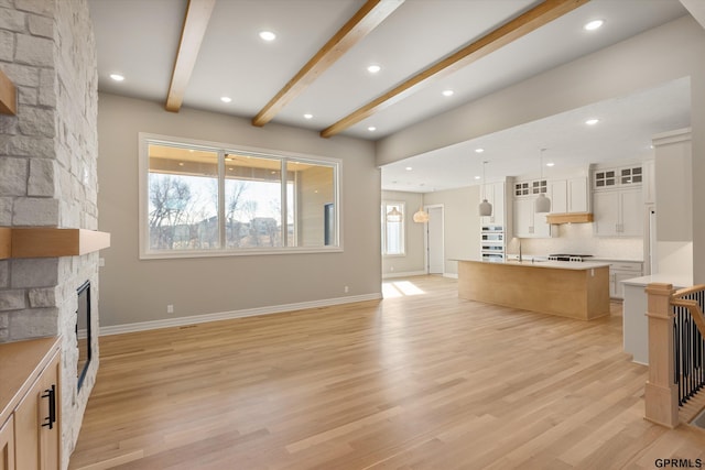 living room with recessed lighting, baseboards, light wood-style floors, beamed ceiling, and a stone fireplace