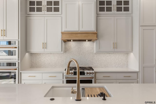 kitchen featuring decorative backsplash, white double oven, light countertops, range with gas cooktop, and premium range hood