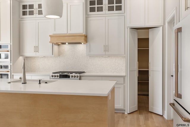 kitchen with light countertops, a sink, glass insert cabinets, white cabinets, and range with gas cooktop