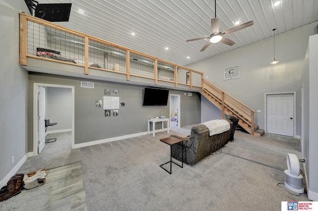 carpeted living room with stairway, a ceiling fan, baseboards, visible vents, and a towering ceiling