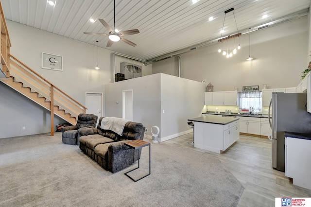 living room with a high ceiling, a ceiling fan, light wood-style floors, and stairs