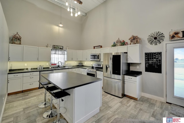 kitchen featuring light wood finished floors, stainless steel appliances, dark countertops, a sink, and a high ceiling