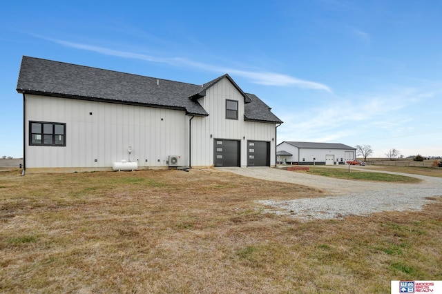 rear view of property featuring gravel driveway, a yard, a shingled roof, and board and batten siding