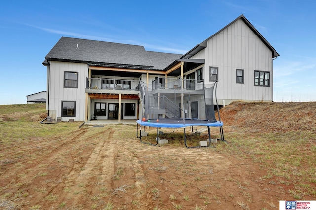 back of house featuring stairs, board and batten siding, a trampoline, a shingled roof, and a patio area