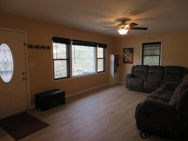 living area featuring baseboards, a ceiling fan, and light wood finished floors