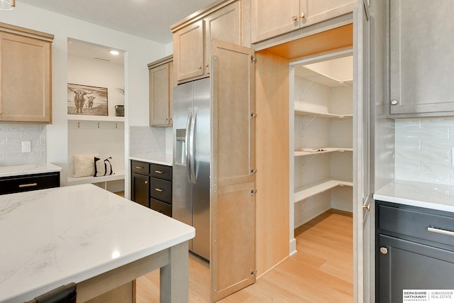 kitchen with light wood finished floors, tasteful backsplash, recessed lighting, light stone counters, and stainless steel fridge with ice dispenser