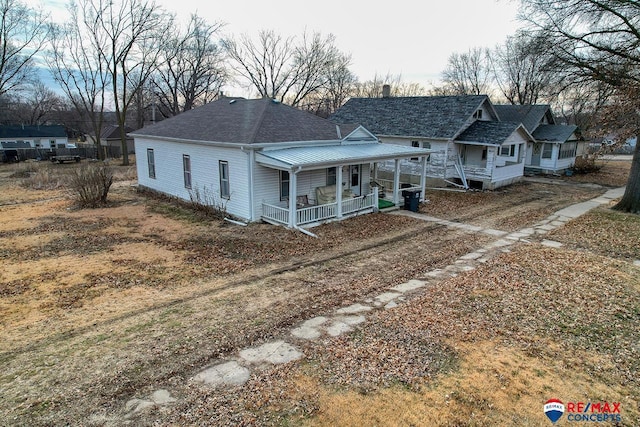 view of front facade featuring covered porch, roof with shingles, and a chimney