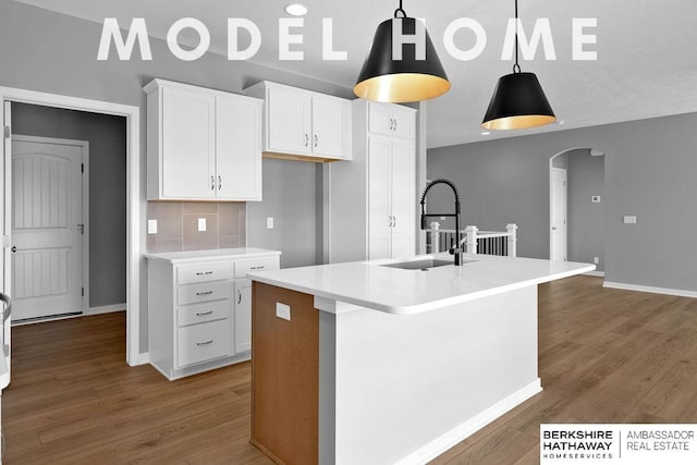 kitchen with white cabinetry, a sink, arched walkways, and wood finished floors