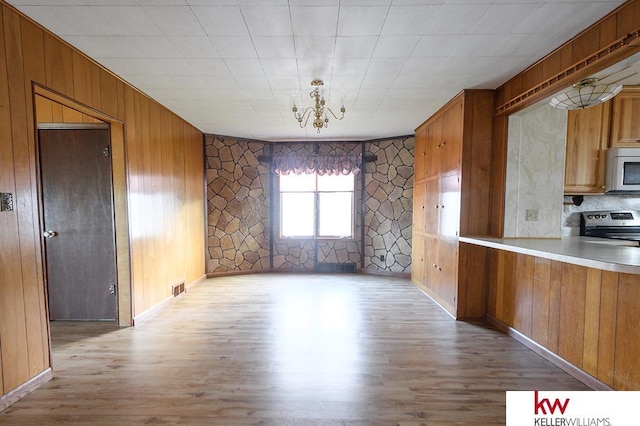 unfurnished dining area with wooden walls, a notable chandelier, light wood finished floors, baseboards, and visible vents