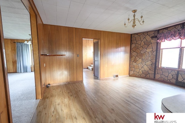 unfurnished room featuring visible vents, wood walls, and a chandelier