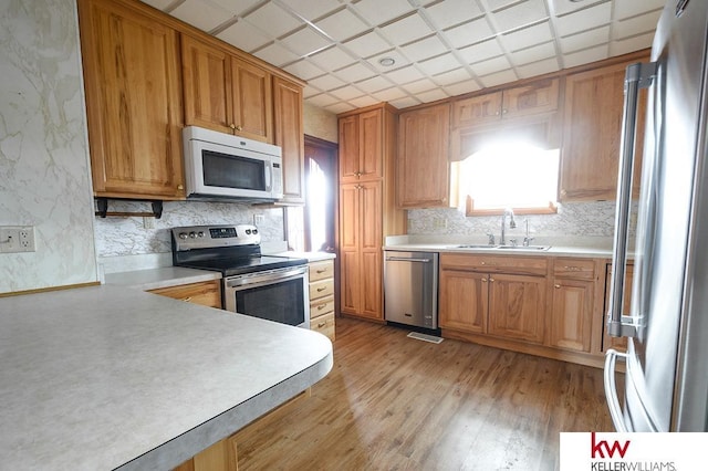 kitchen featuring a sink, light countertops, light wood-style flooring, stainless steel appliances, and tasteful backsplash