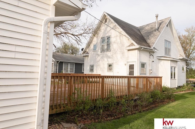 rear view of house featuring roof with shingles, a lawn, and a deck