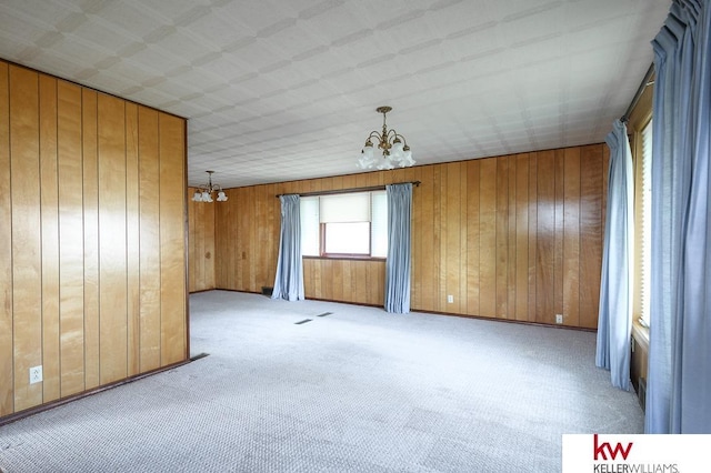 unfurnished room with carpet flooring, wood walls, and a chandelier